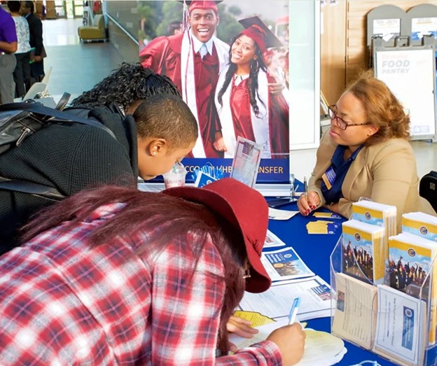 Black woman sits at a table as a student fills out a form