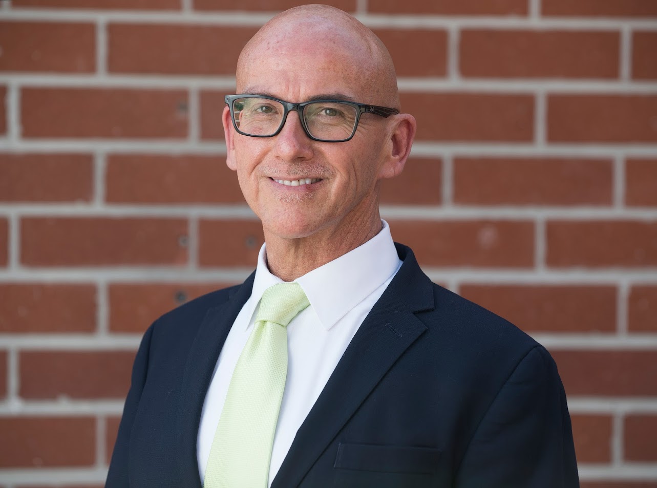 Portrait of white bald man wearing a suit against a brick backdrop