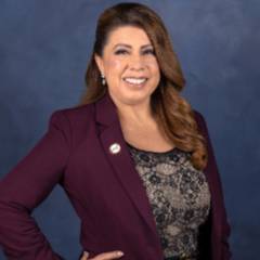 Portrait of Dr Martha Garcia, wearing a burgundy suit, posed with her hands on her hips