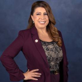 Portrait of Dr Martha Garcia, wearing a burgundy suit, posed with her hands on her hips