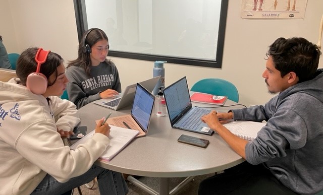 three students seated at a table studying